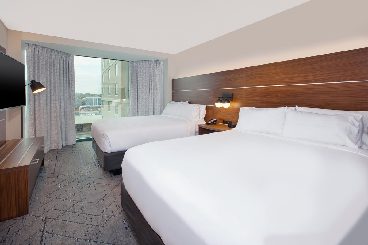 Een hotelkamer met twee bedden, een televisie, een bureau en een raam met gordijnen.