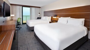 A hotel room with two beds, a desk, a chair, a TV, and a balcony with curtains. - Holiday Inn Express & Suites VA Beach Oceanfront by IHG (Virginia Beach)