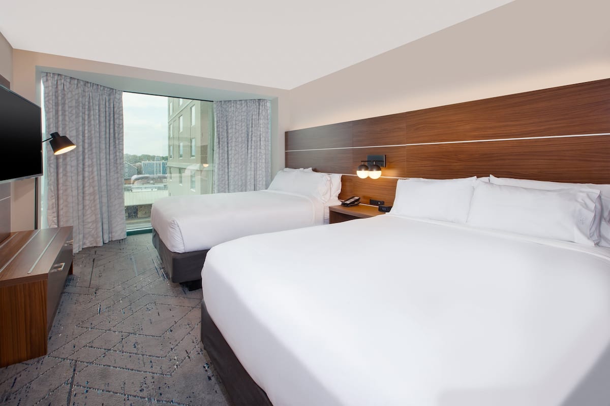 A hotel room with two beds, a TV, a desk, and a window with curtains.