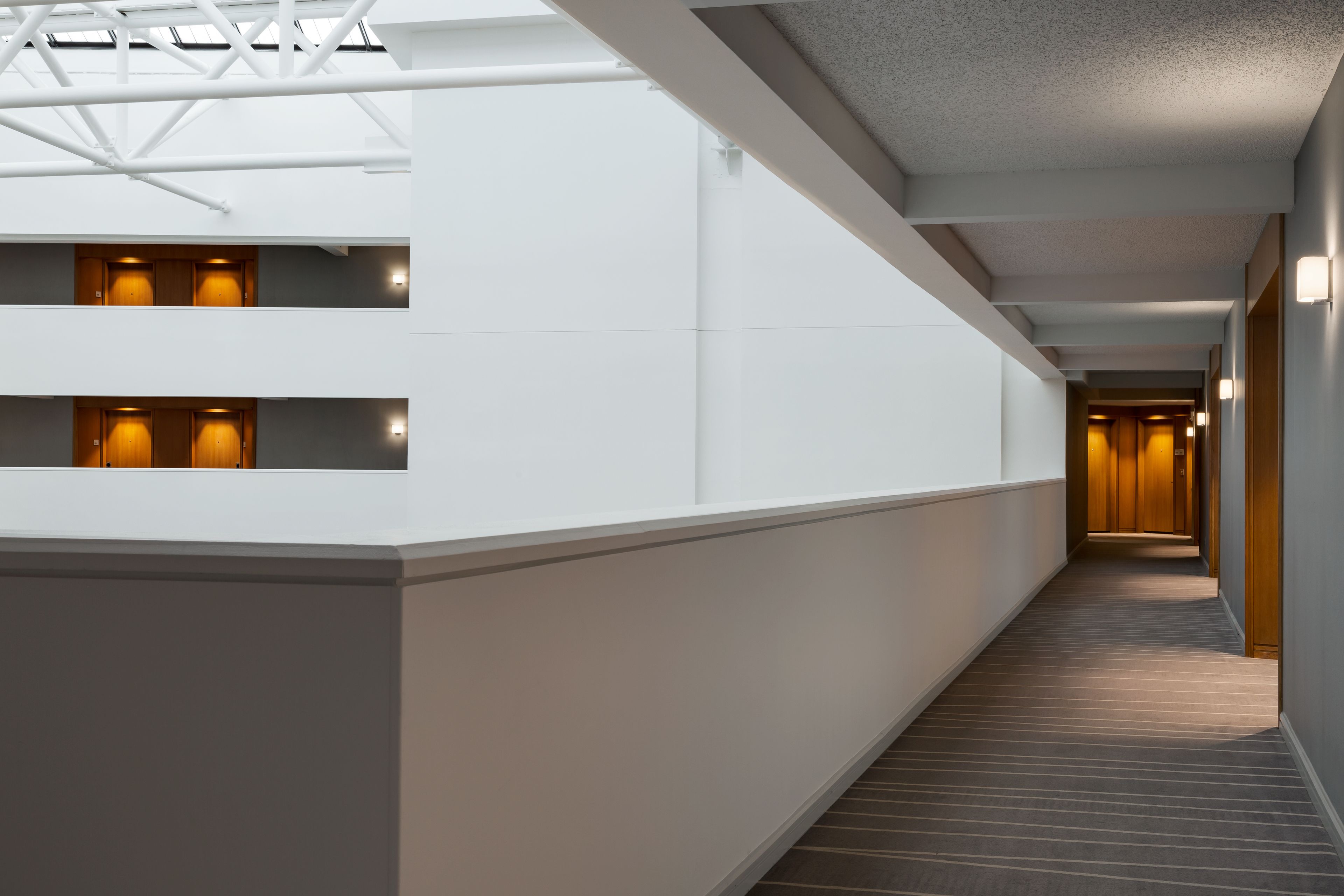 A modern hotel corridor with a straight layout, white walls, and a wooden floor.