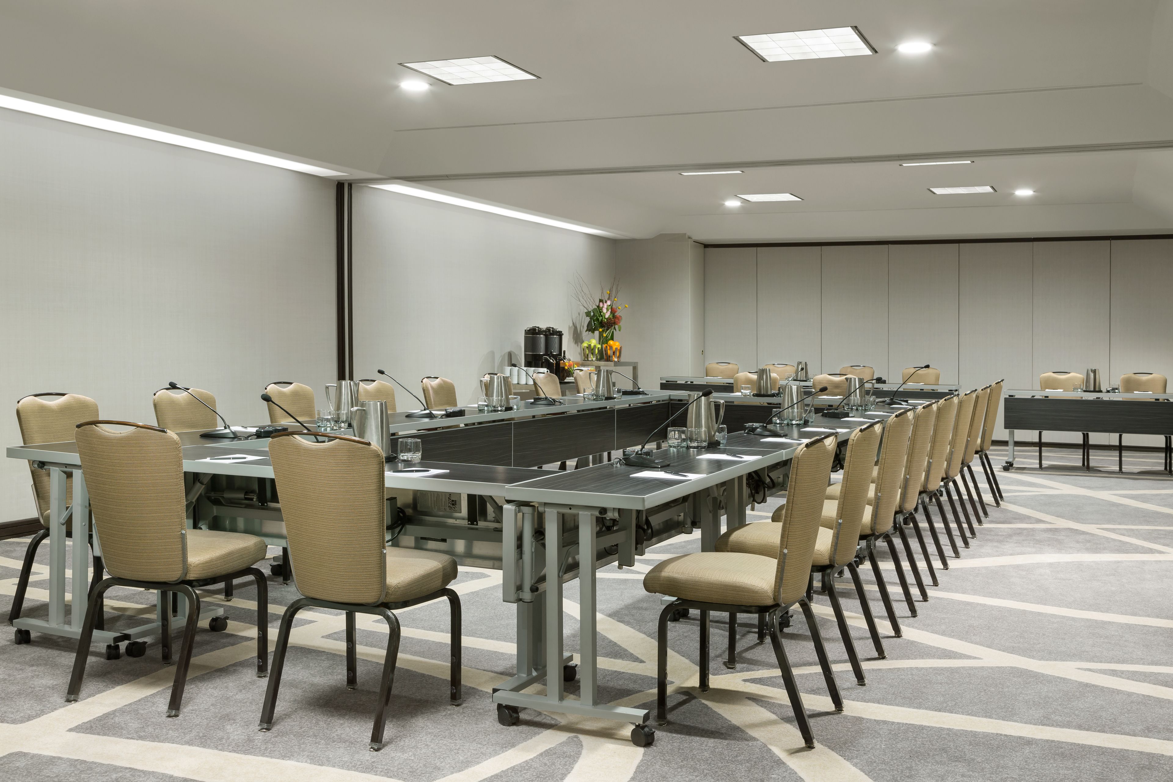 Un salón de conferencias con una larga mesa, sillas y una estación de café.
