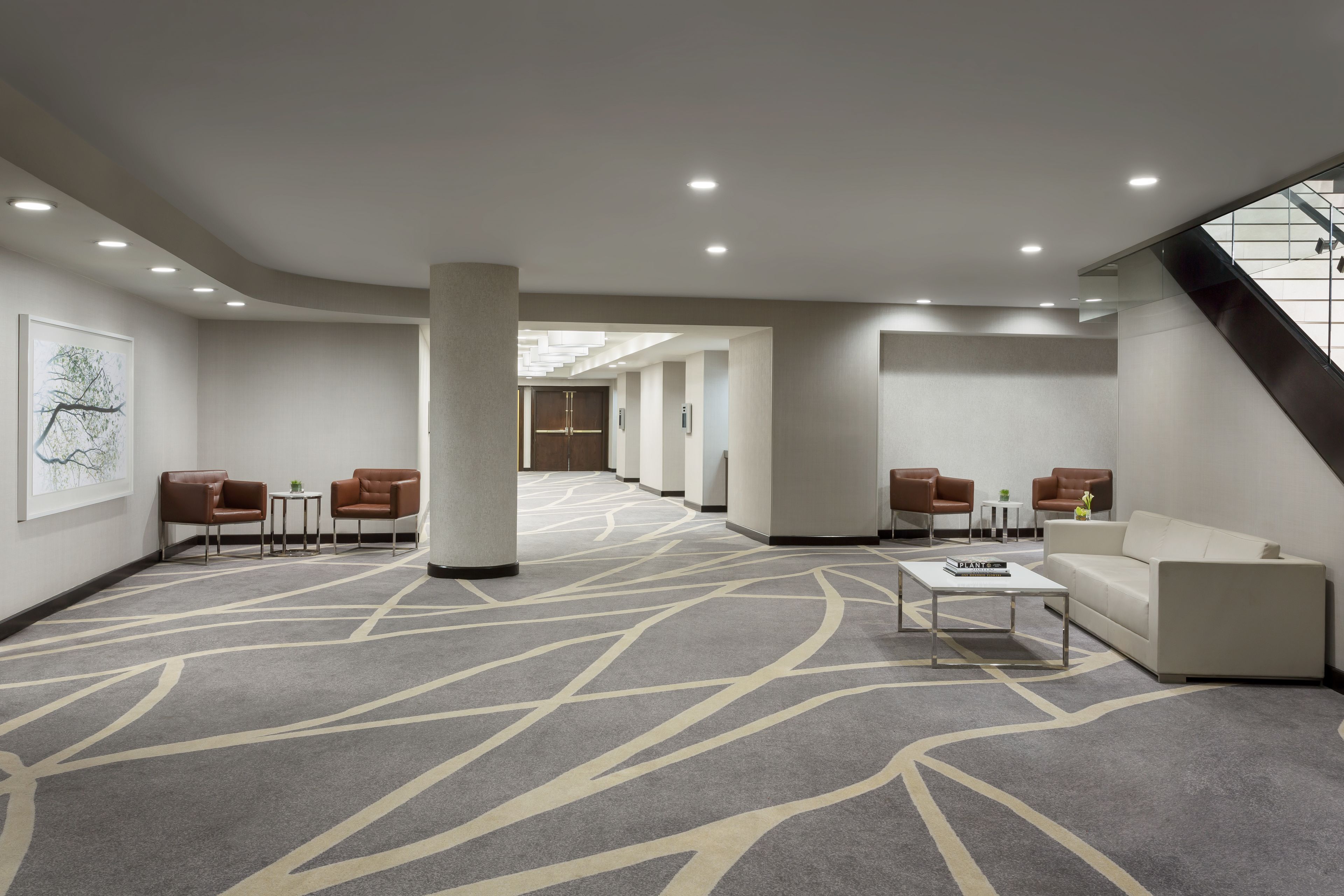 Un hall d’hôtel moderne, doté d’un sol recouvert de moquette, d’espaces aménagés avec des sièges et d’un escalier.