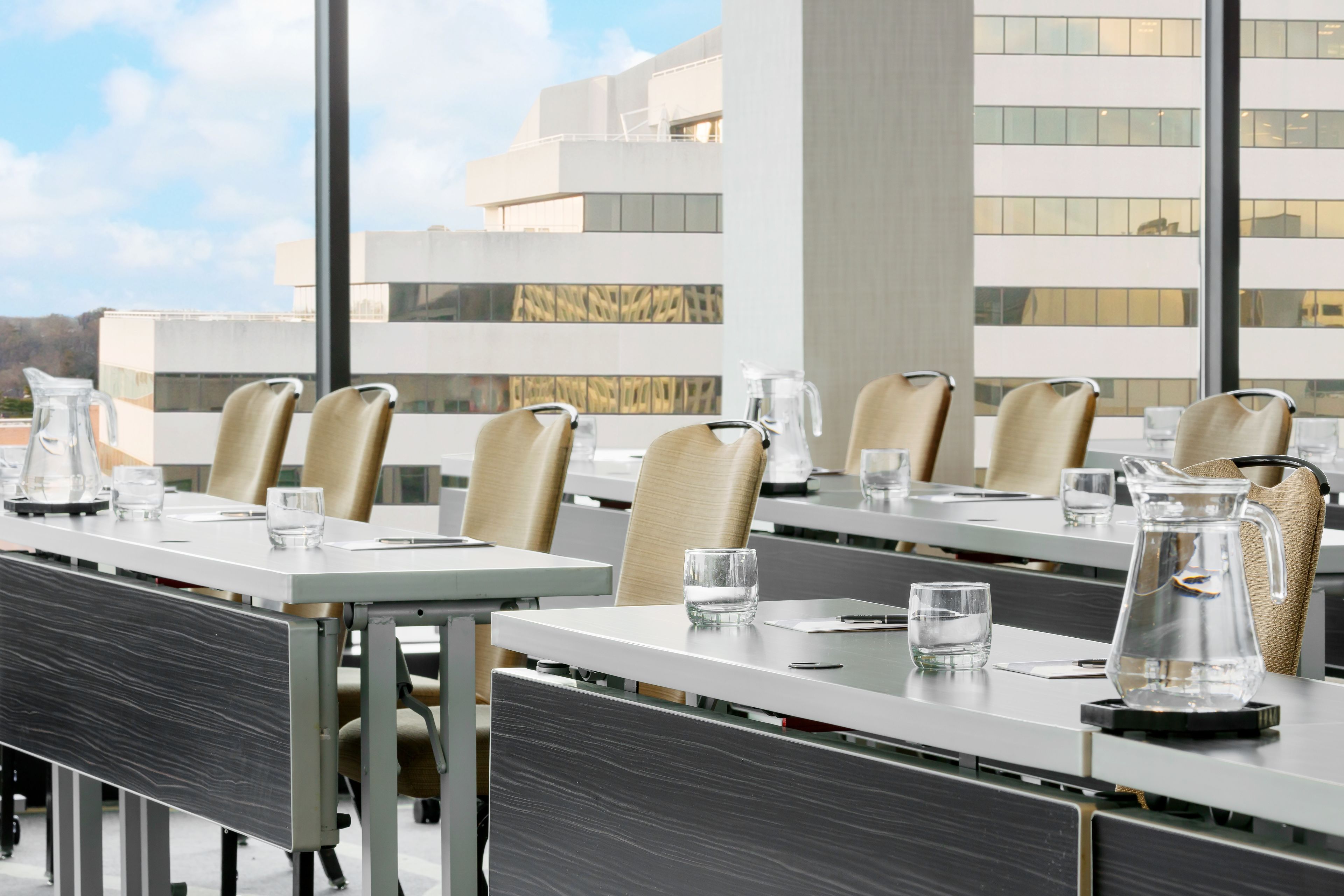 A conference room with tables and chairs, large windows, and a view of a modern building.