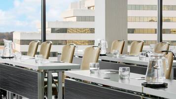 A conference room with tables and chairs, large windows, and a view of a modern building.