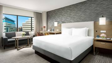 A hotel room with a large bed, a desk, a sofa, and a view of buildings.