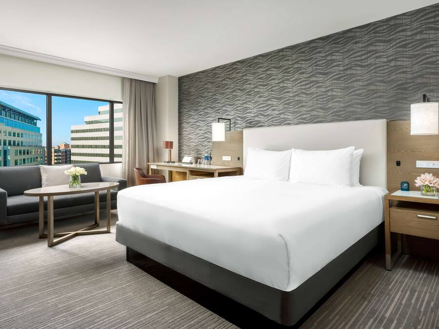 A hotel room with a large bed, a desk, a sofa, and a view of buildings.