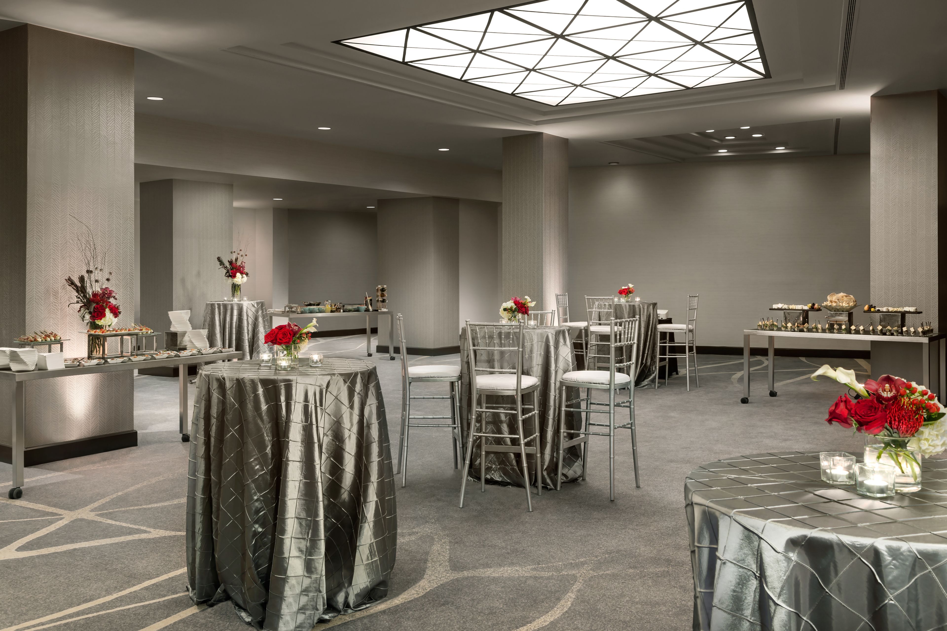 A spacious hotel lobby with multiple round tables, chairs, and a high ceiling with a skylight.