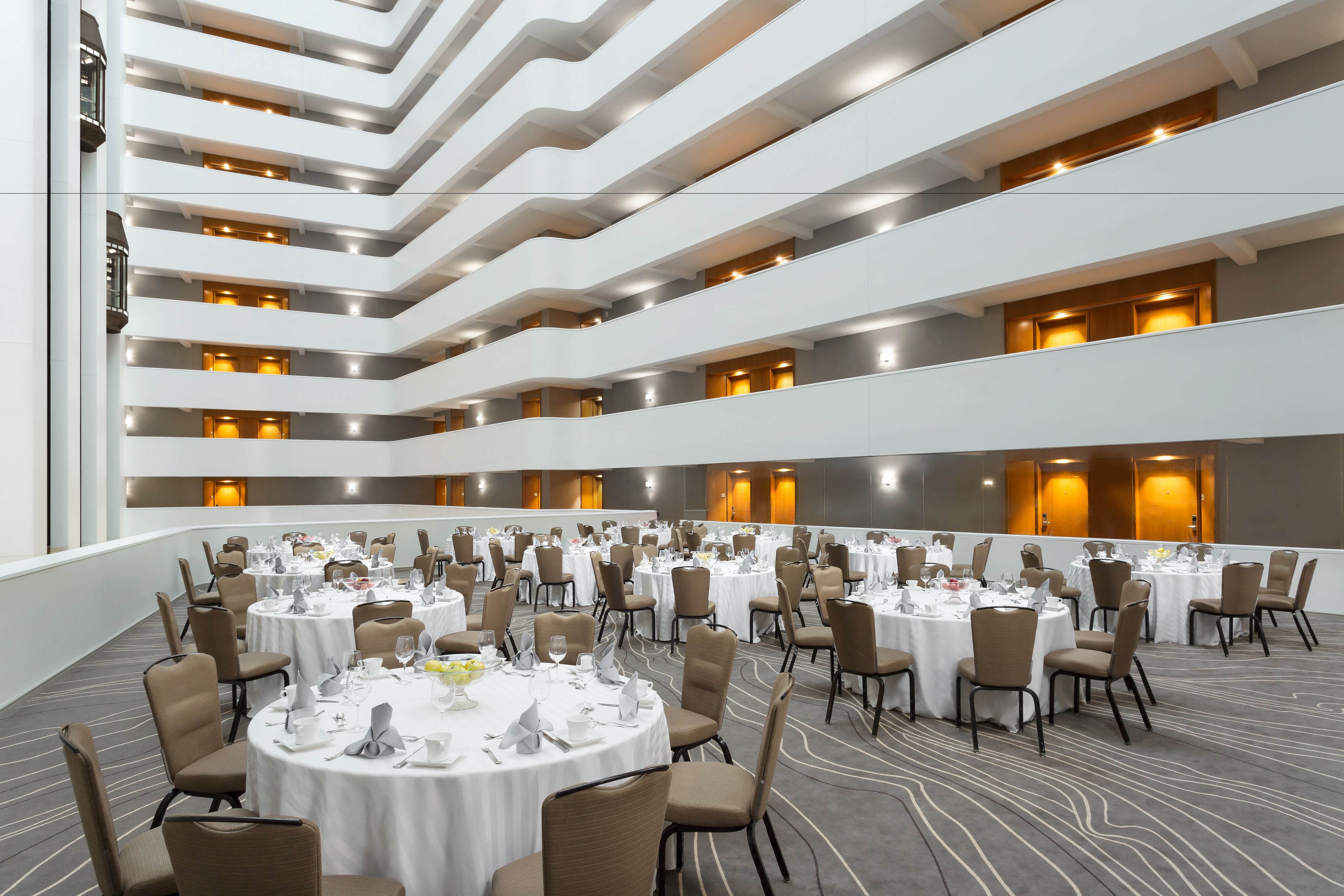 A multi-level dining area with round tables and chairs, featuring a modern architectural design with exposed ceilings and warm lighting.