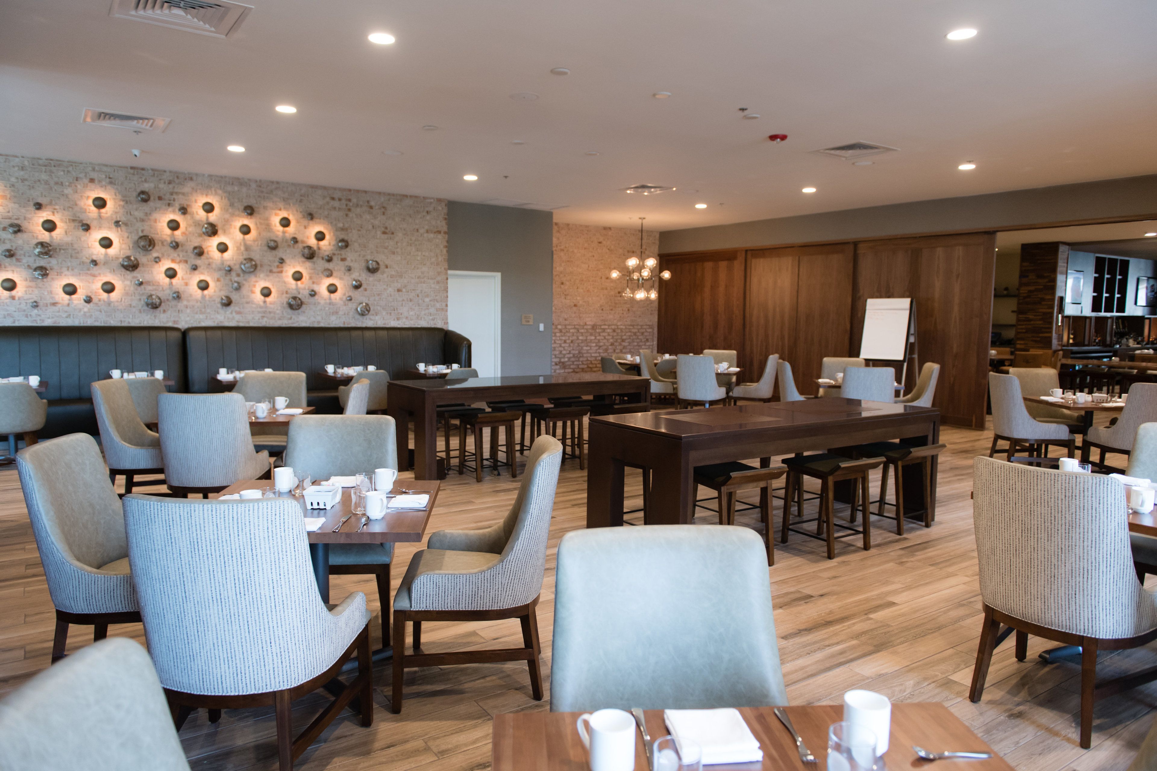 Un espace repas moderne avec plusieurs tables et chaises, un mur de briques orné de motifs circulaires, et une cuisine visible au fond.