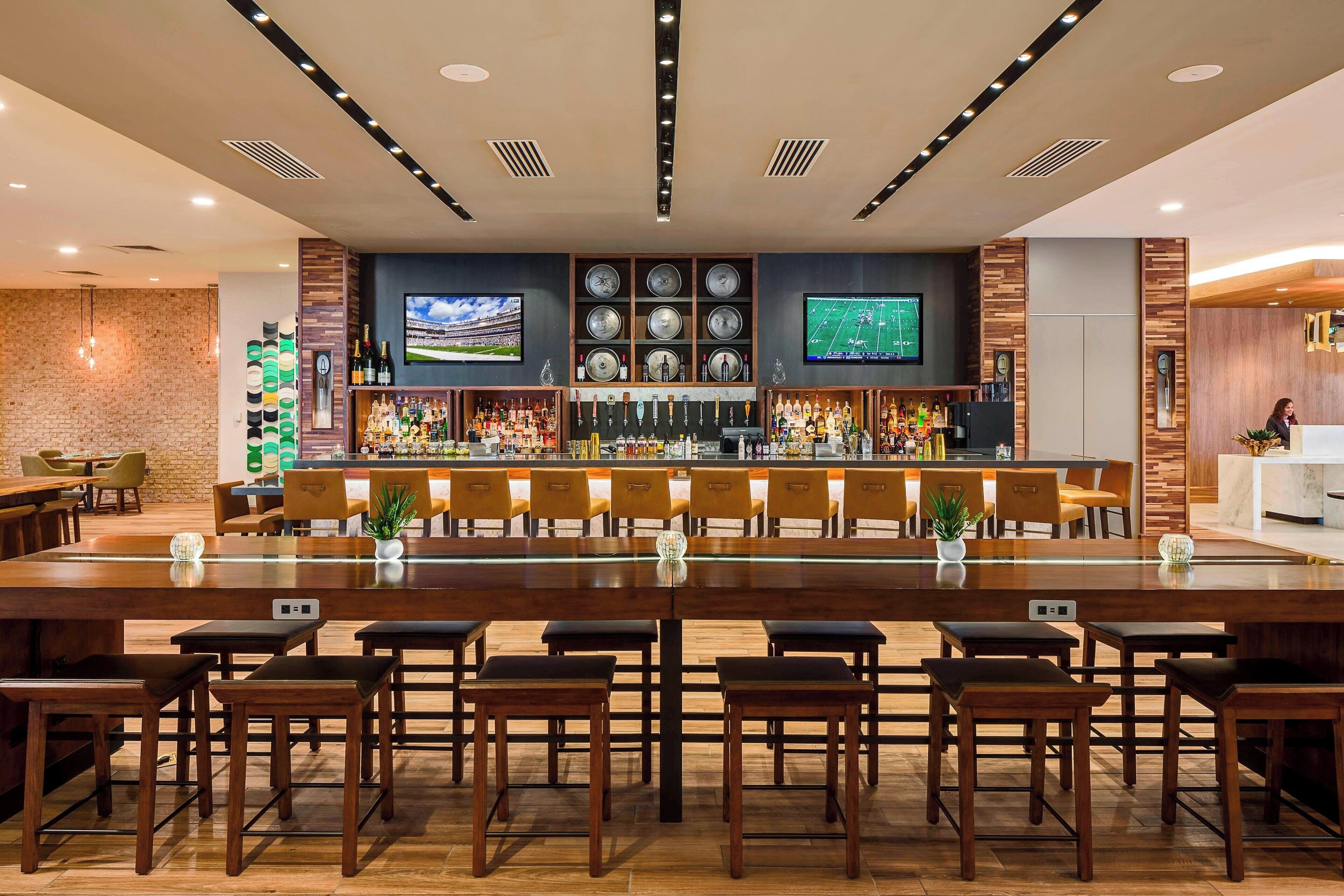 A bar area with a long counter, multiple stools, and a television screen.