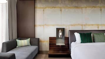 Una habitación de hotel moderna con sofá, cama, mesita de noche y lámpara de pared.