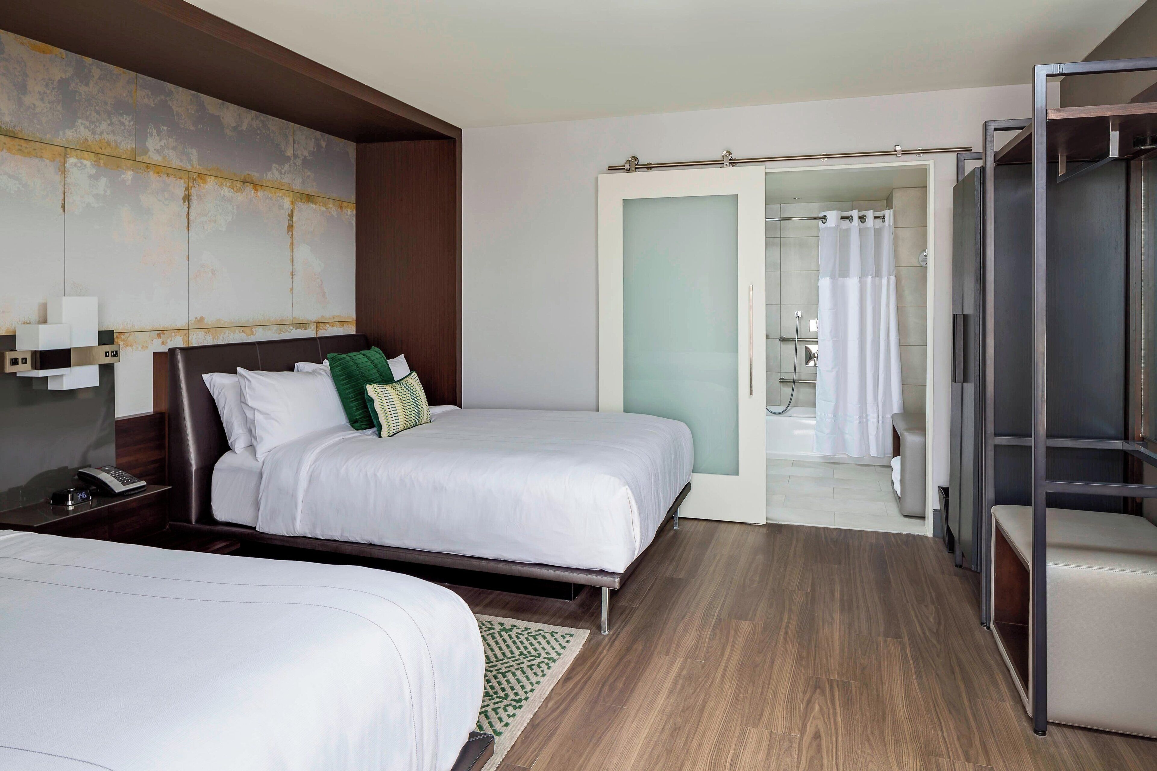 A hotel room with two beds, a large mirror, a wardrobe, and a bathroom visible through an open door.