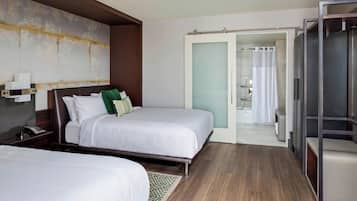 A hotel room with two beds, a large mirror, a wardrobe, and a bathroom visible through an open door.