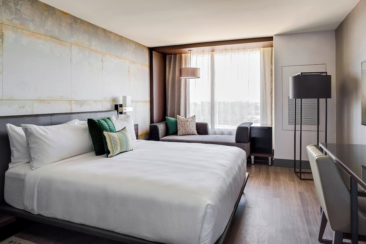 A hotel room with two beds, a desk, and a large window with curtains.