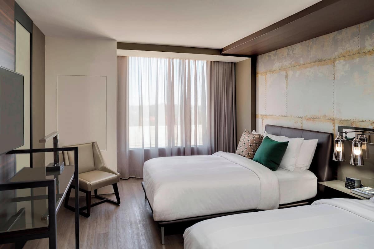 A hotel room with two beds, a desk, and a chair.