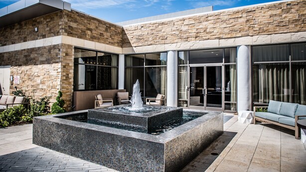A modern building with a stone facade, a water feature, outdoor seating, and large windows. - North Charleston Marriott (North Charleston)