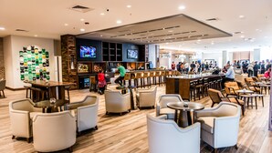A spacious bar area with multiple seating options and a television screen displaying a sports event. - North Charleston Marriott (North Charleston)