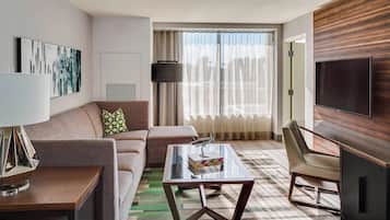 Une chambre d’hôtel moderne, dotée d’un canapé, d’une table basse en verre, d’un téléviseur et d’une grande fenêtre avec des rideaux.