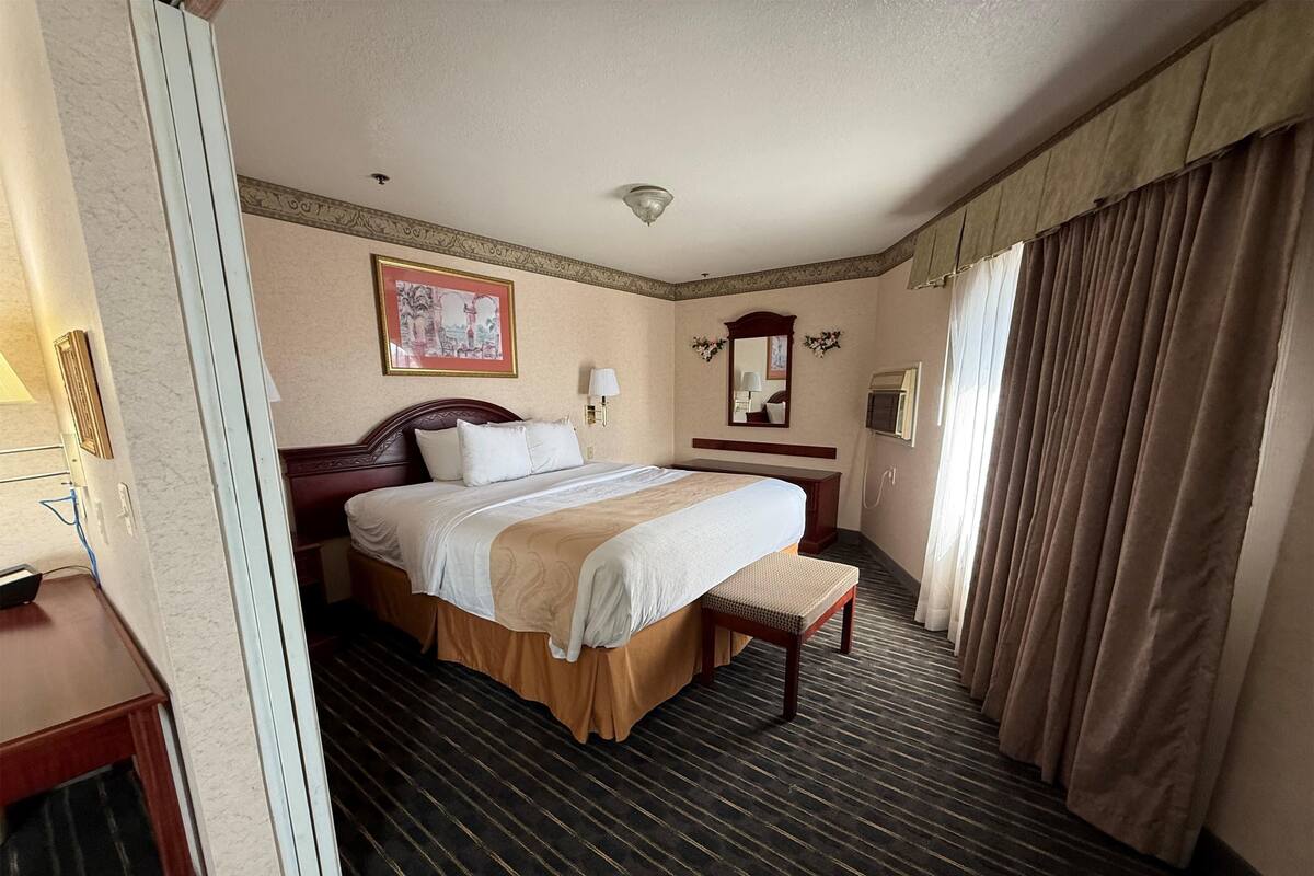 A hotel room with a large bed, a bedside table, a mirror, and a window with curtains.