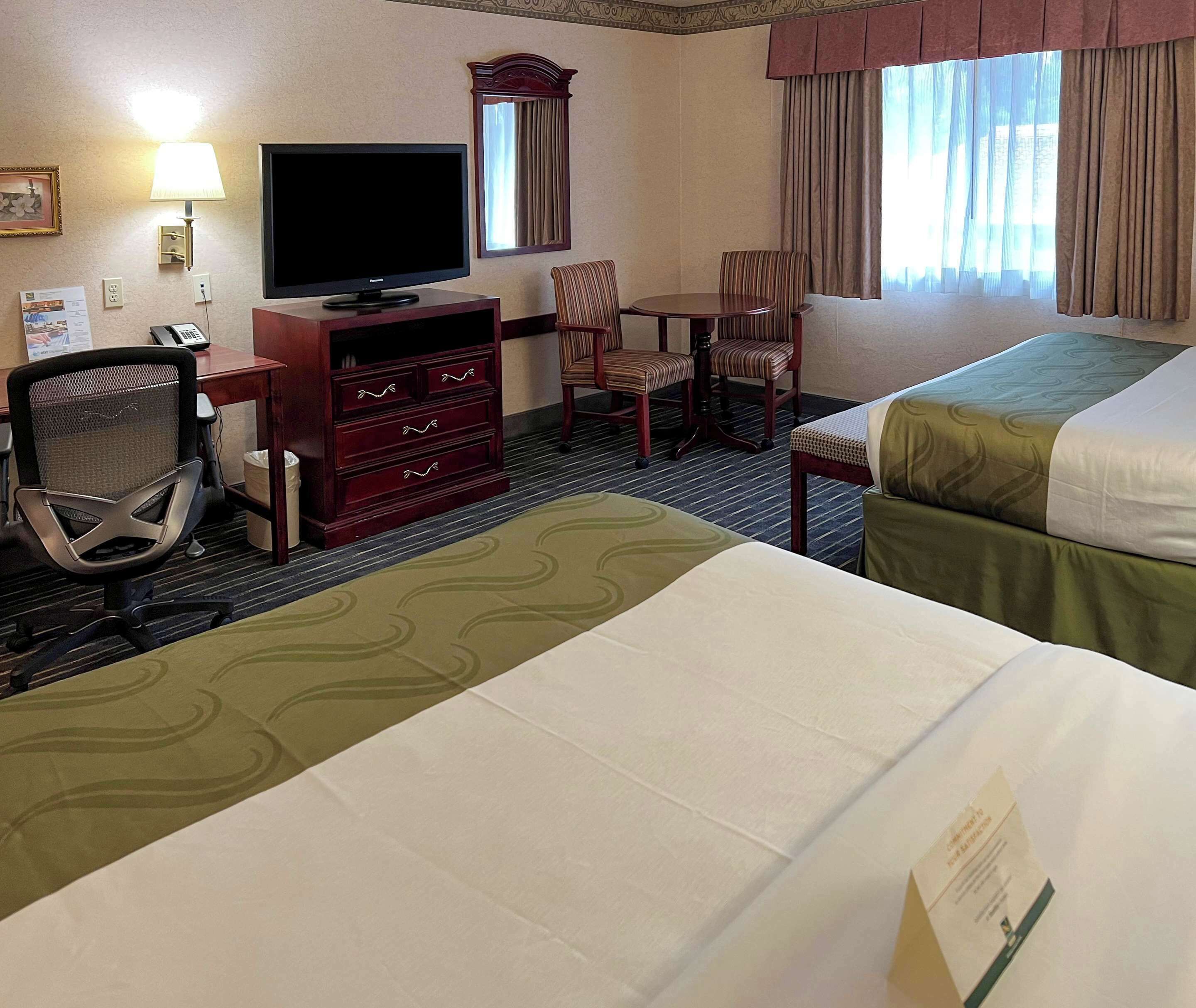 Une chambre d’hôtel comprenant un lit, un bureau avec un ordinateur, une chaise, une télévision et une fenêtre avec des rideaux.
