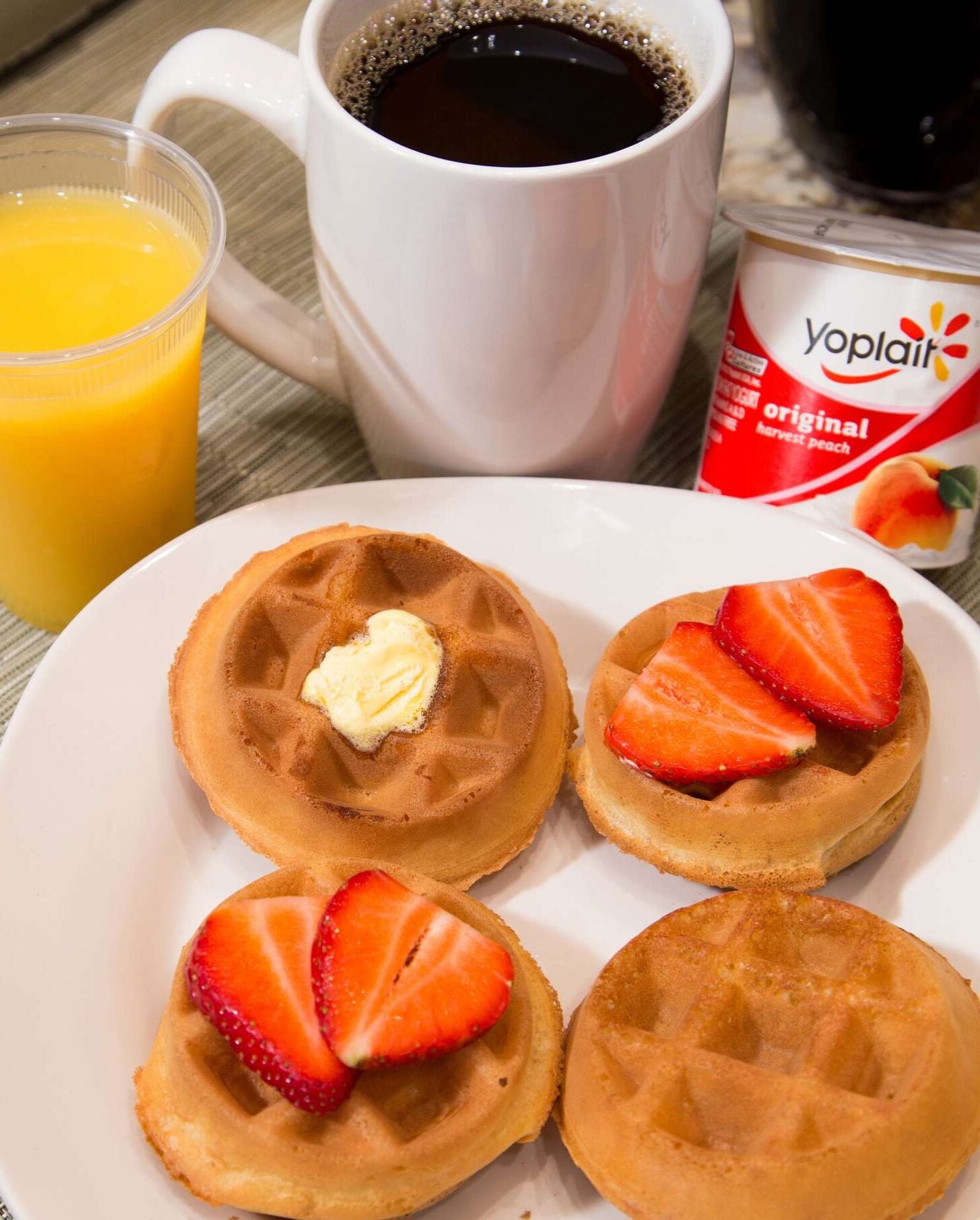 A plate of waffles with strawberries and a cup of coffee.