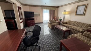 Een hotelkamer met een flatscreen televisie, een bureau, een zwarte bureaustoel, een bank en een lamp.