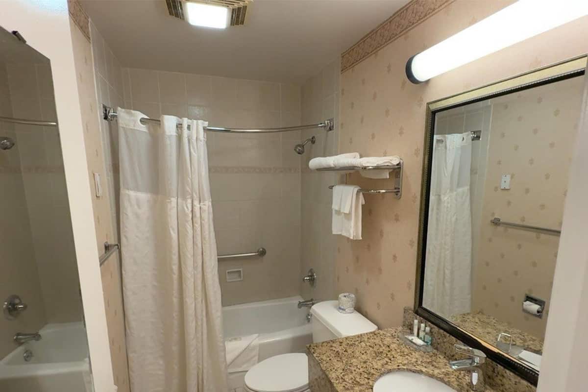 A bathroom with a shower, toilet, and sink, featuring a large mirror and towel rack.