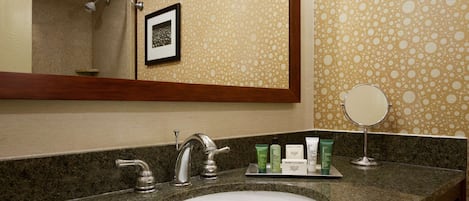 A bathroom with a granite countertop, a sink, a mirror, and toiletries.