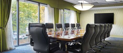 A conference room with a long table, multiple chairs, and a large window with curtains.
