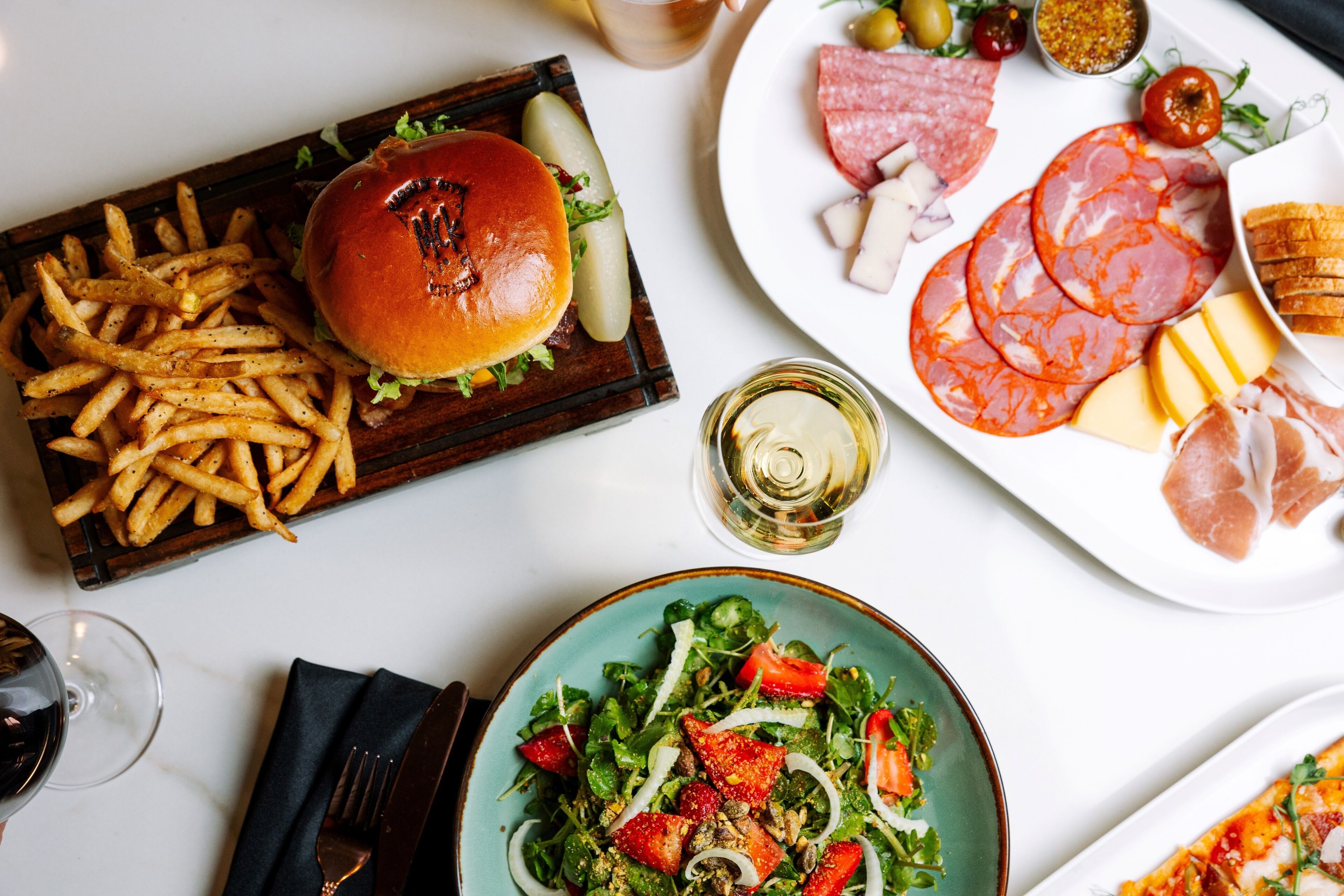 Une table avec un hamburger, des frites, une salade et différentes sortes de viande.