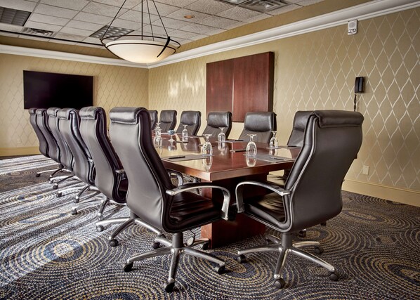 A conference room with a large table, multiple chairs, and a patterned carpet.