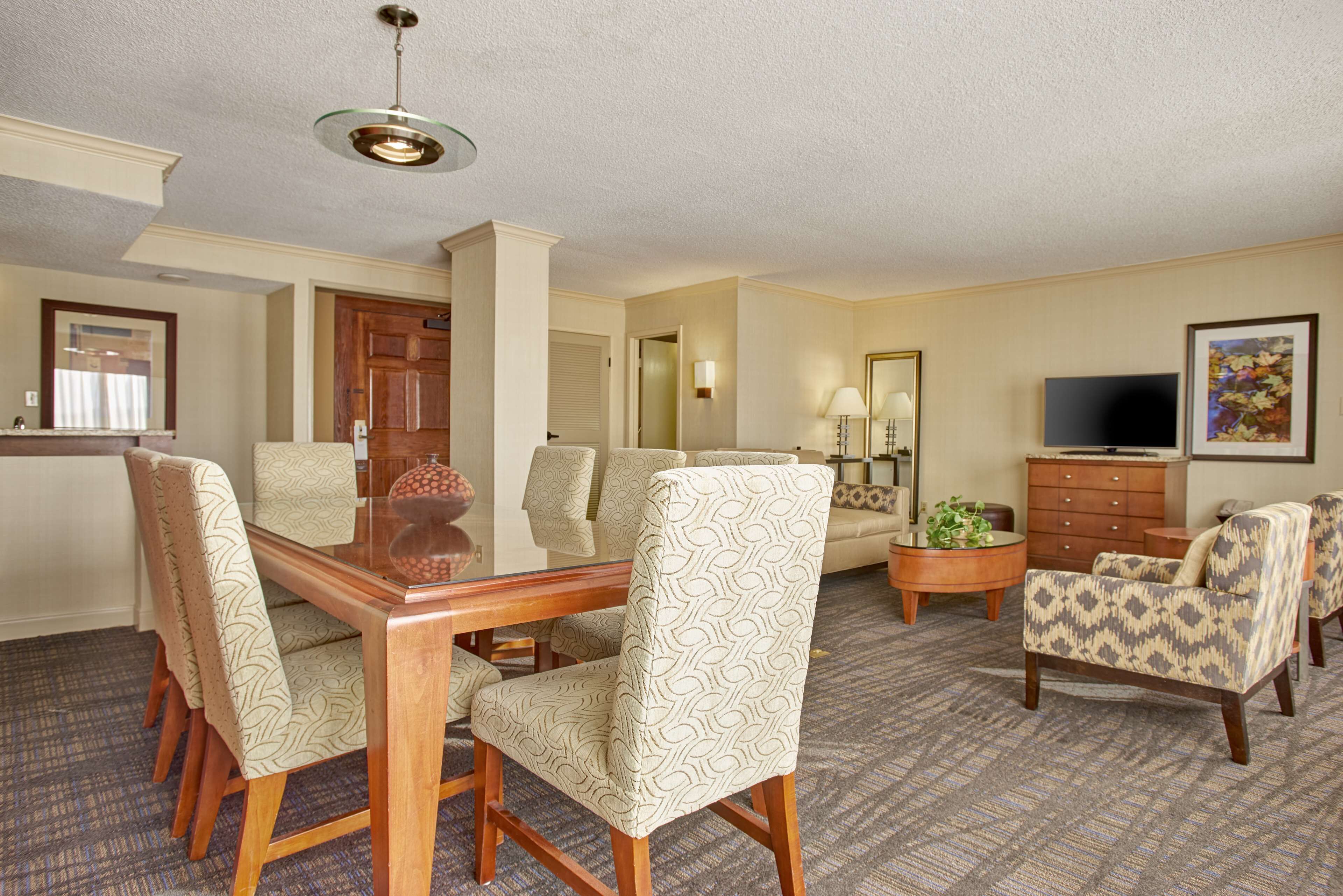 A dining area with a wooden table and chairs, a sofa, a TV, and a mirror.