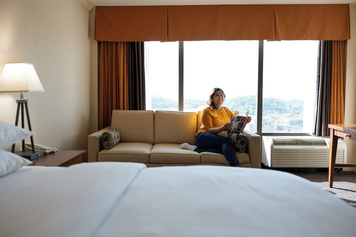 Een hotelkamer met een bed, een slaapbank, een lamp en een raam met gordijnen.