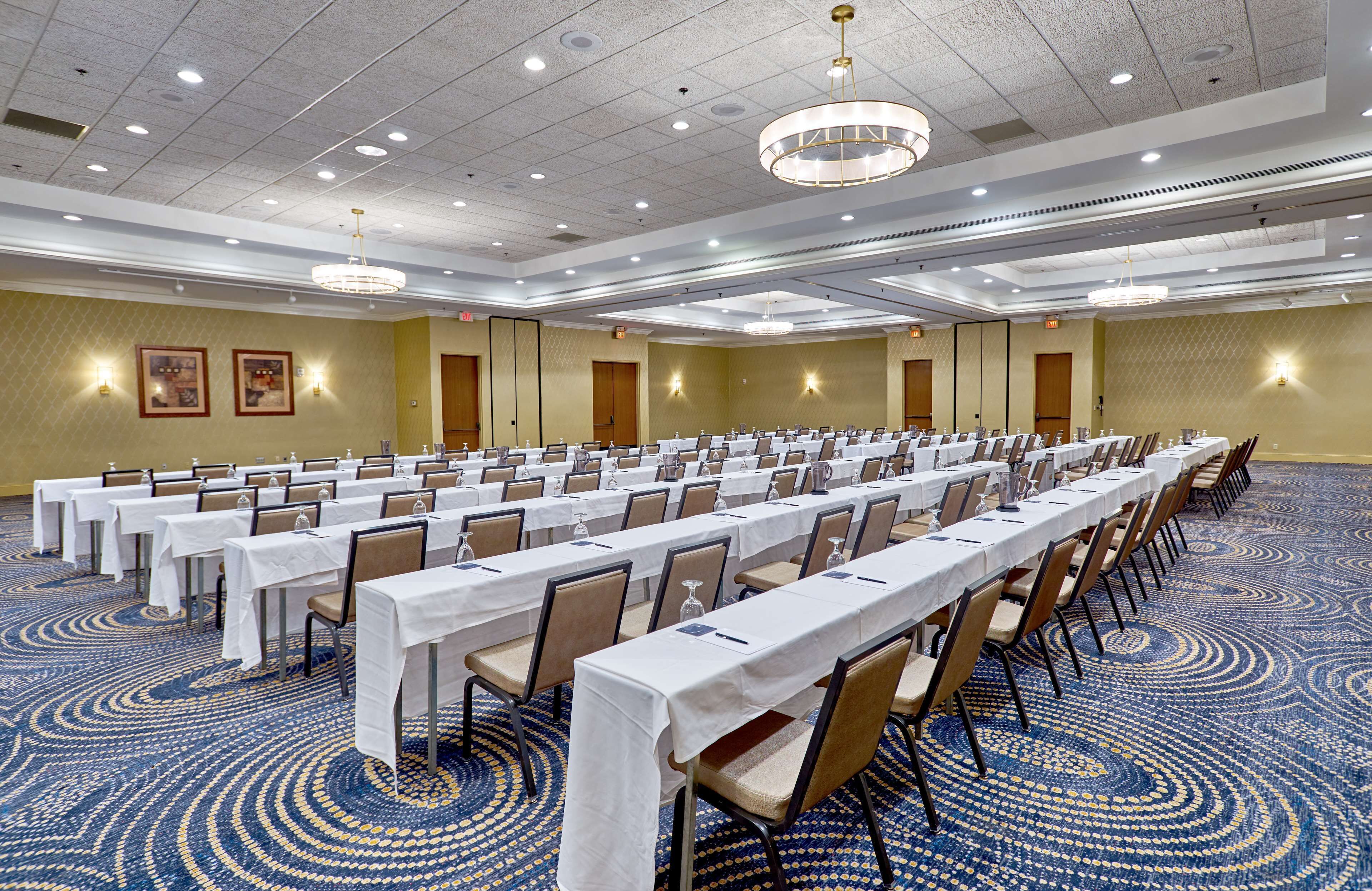 A large conference room with rows of tables and chairs, equipped with water bottles and nameplates.