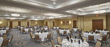 A large banquet hall with multiple round tables set for dining, equipped with chairs and table settings.