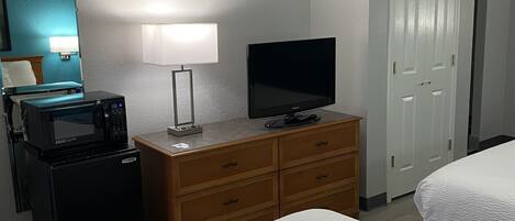 A hotel room with a bed, a TV, a microwave, a dresser, a lamp, and a door.
