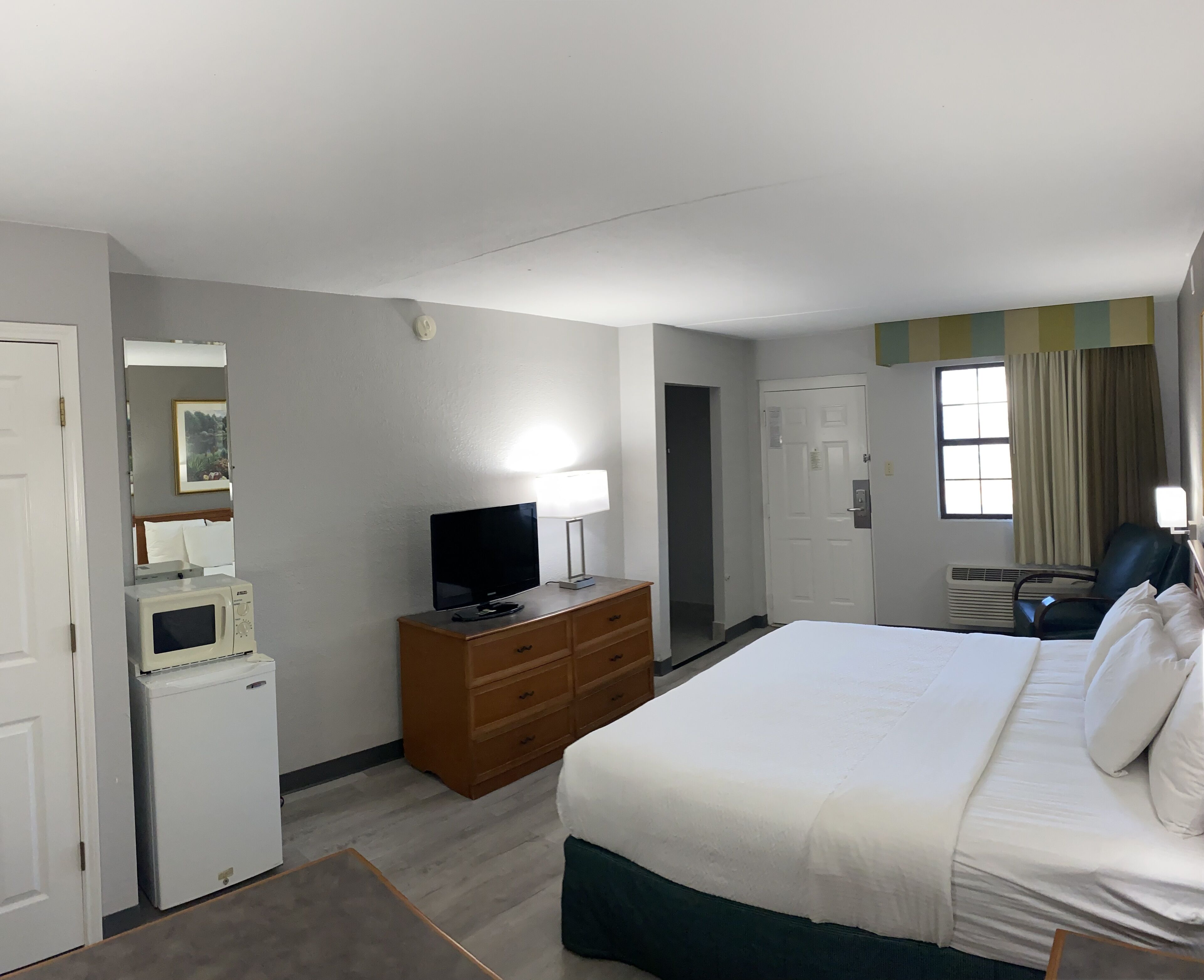 A hotel room with a bed, a television on a wooden dresser, a microwave, and a window with curtains.