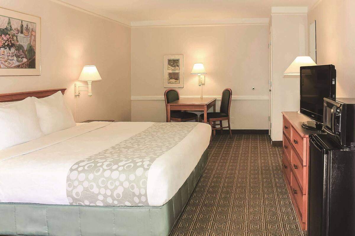 Une chambre d’hôtel comprenant un lit, un bureau, deux chaises, une télévision et une commode.