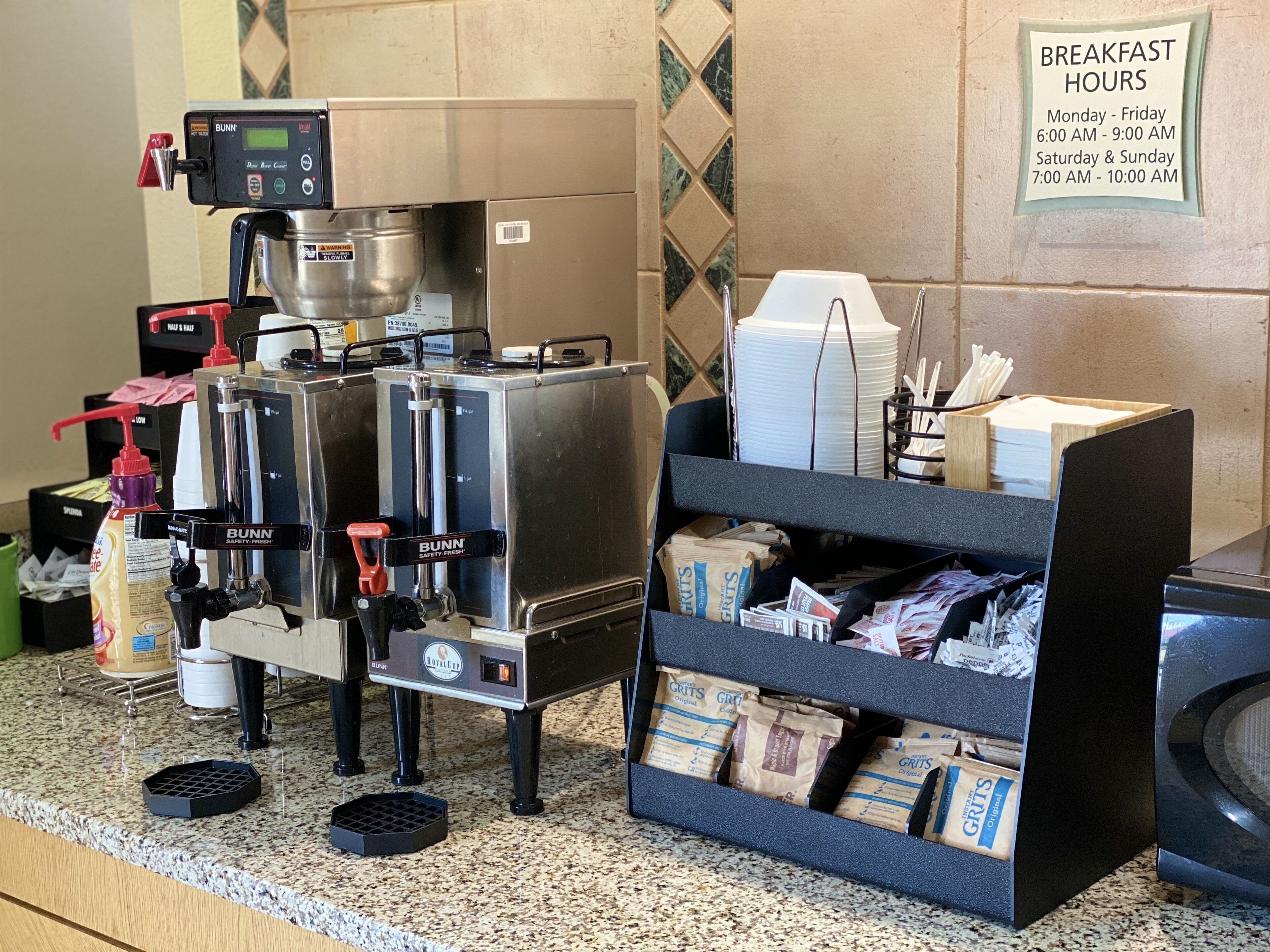 Una cafetera, un letrero que indica los horarios del desayuno y un estante con paquetes de café.