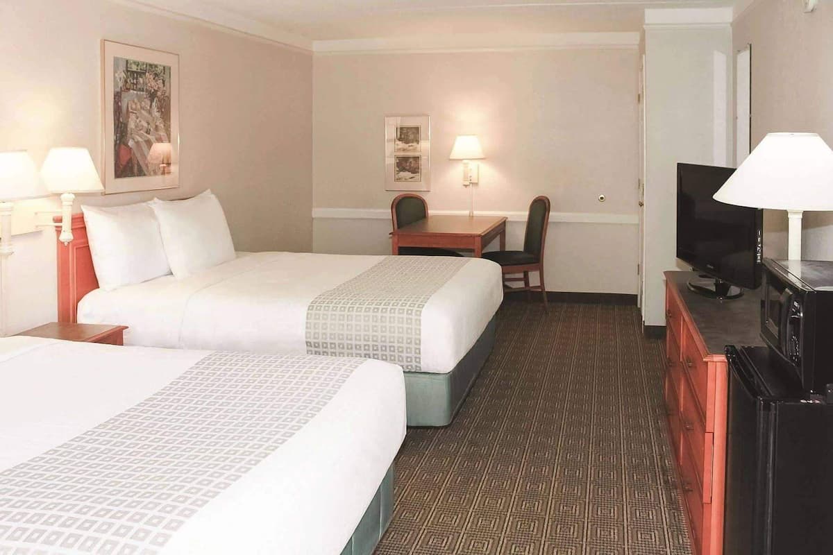 Une chambre d’hôtel avec deux lits, un bureau, une chaise, une télévision et un four à micro-ondes.