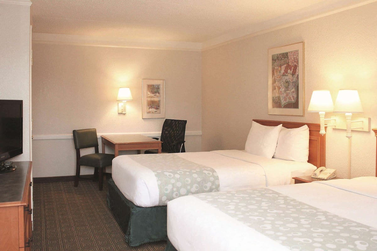 Une chambre d’hôtel avec deux lits, un bureau, une chaise, une télévision et un téléphone.