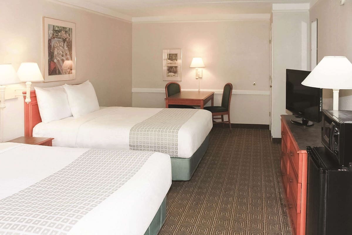 Une chambre d’hôtel avec deux lits, un bureau, une chaise, une télévision et une lampe.