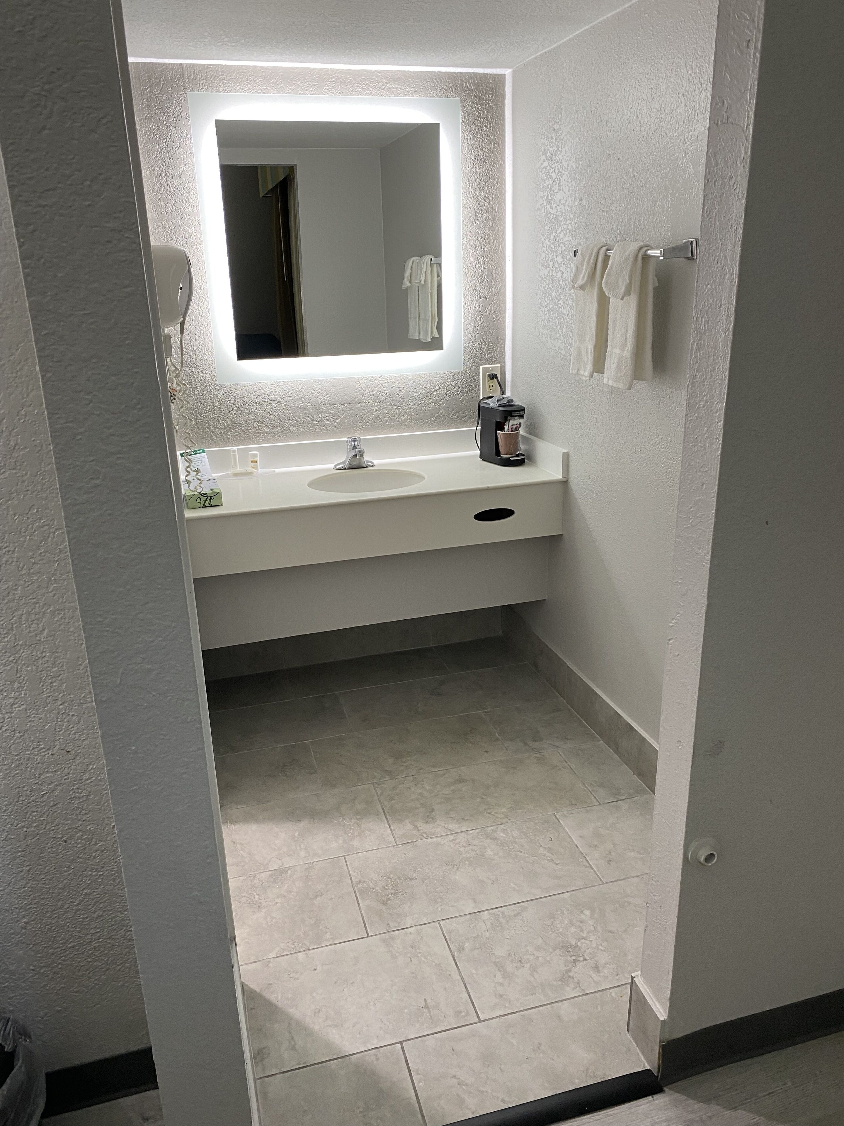 Un baño con lavamanos blanco, espejo y toallero.