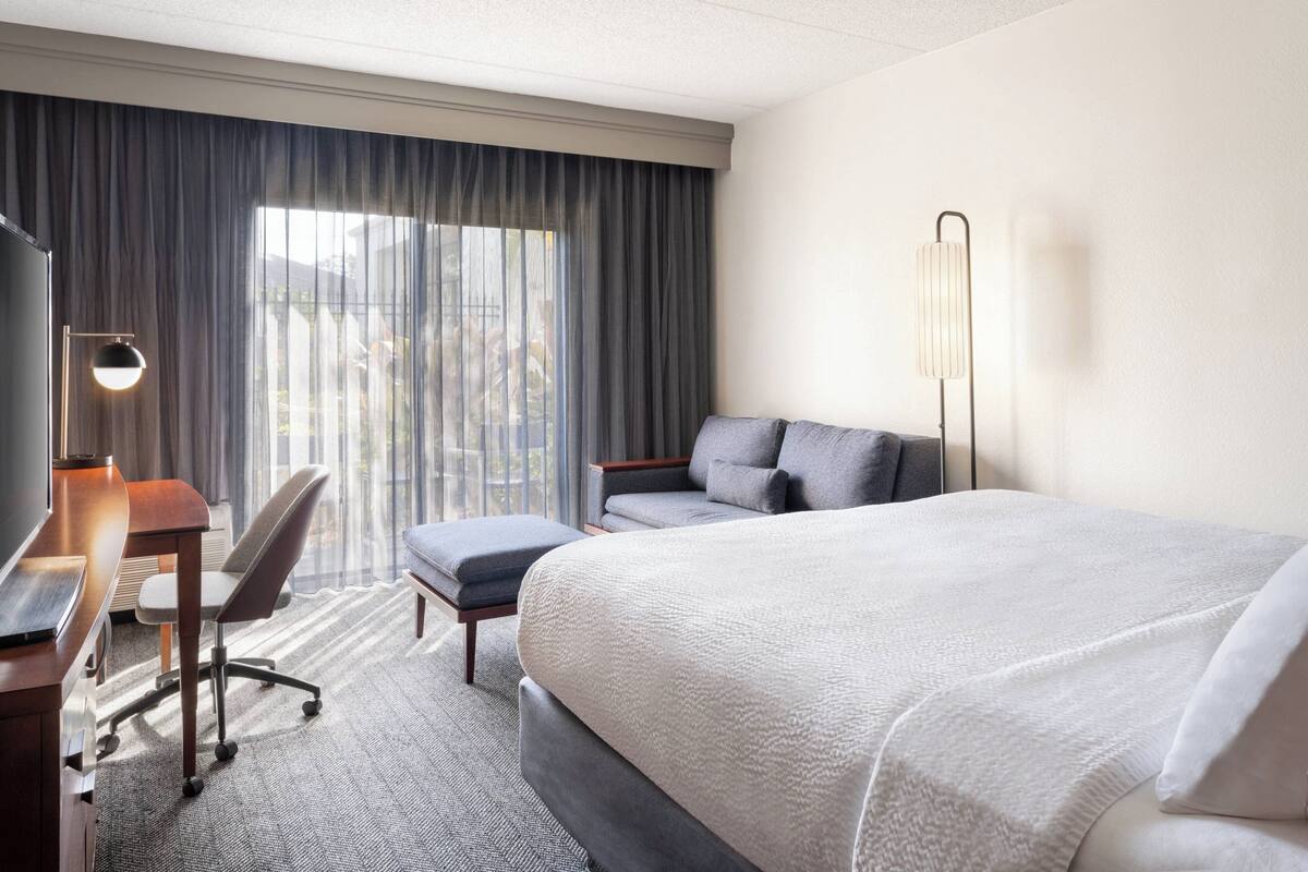 Ein Hotelzimmer mit einem großen Bett, einem Schreibtisch mit Stuhl, einer Couch und einer Stehlampe.