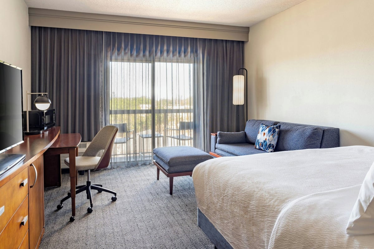 Ein Hotelzimmer mit Bett, Schreibtisch mit Stuhl, Fernseher und einem großen Fenster mit Vorhängen.