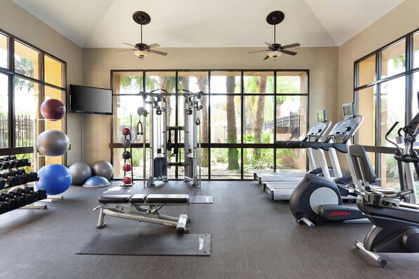 A gym with exercise equipment, large windows, and ceiling fans.