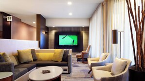 A modern living room with a sectional sofa, armchairs, a flat-screen TV, and a coffee table. - Courtyard by Marriott Tampa Westshore/Airport (Tampa)