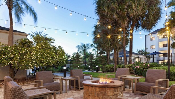 An outdoor patio area with wicker furniture, a stone fire pit, and string lights. - Courtyard by Marriott Tampa Westshore/Airport (Tampa)