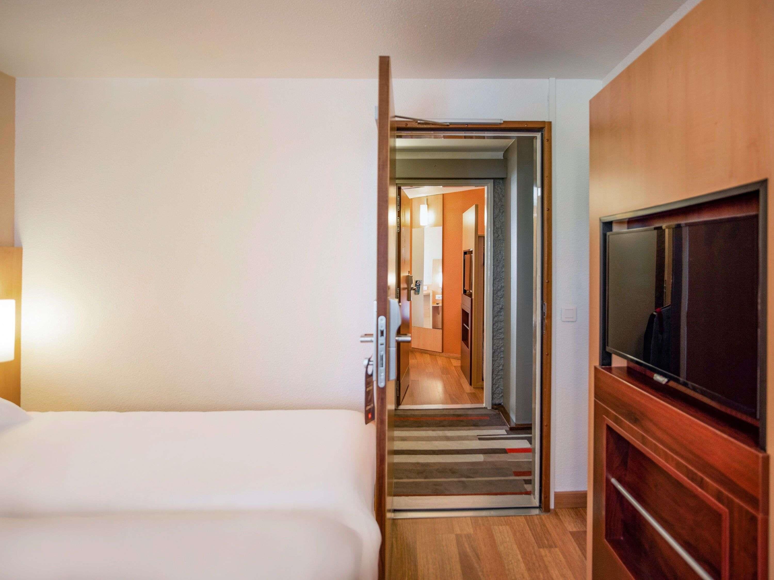 A hotel room with a bed, a television, and a hallway leading to a bathroom.