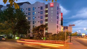 A multi-story hotel with a prominent 'ibis' sign, a parking lot, and a street with light trails. - ibis Tours Centre Gare (Tours)